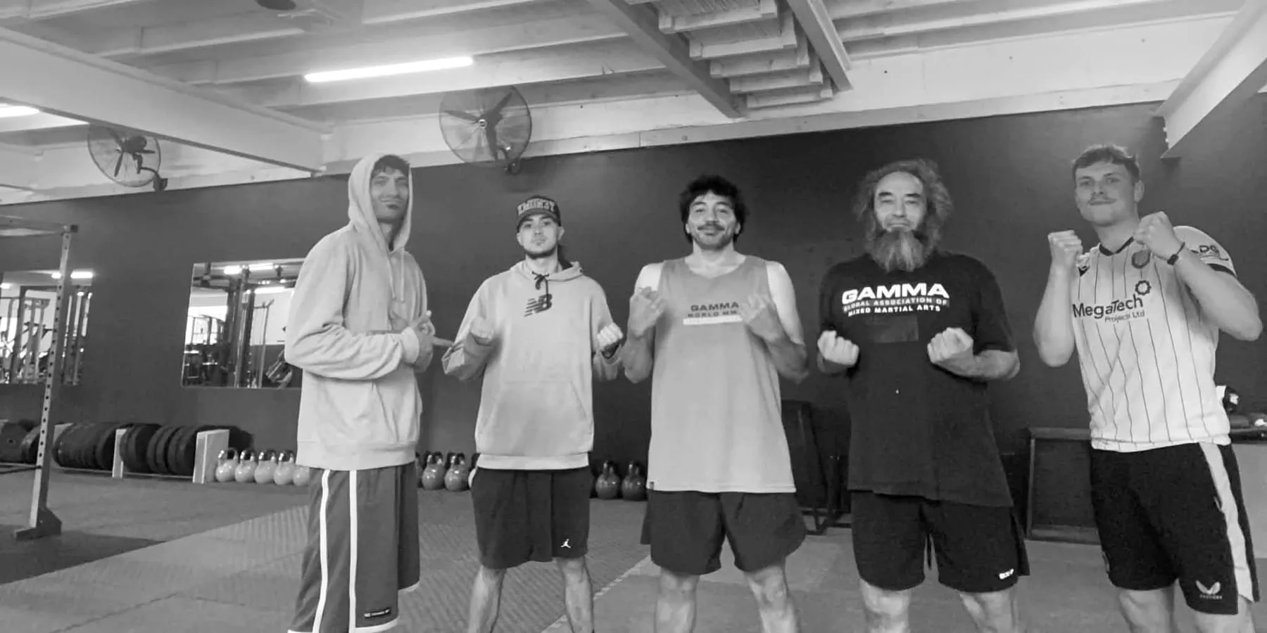 Five Sabretooth Fighters posing on the mats at PURE Movement, most with their fists up, kettlebells and weight plates behind them.