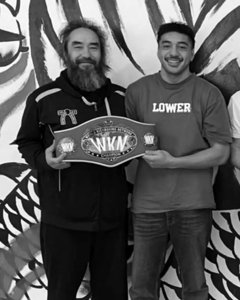 Two Sabretooth Fighters smiling as they hold up a World Kickboxing Network champion belt.